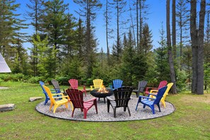 Un’area salotto esterna circolare con un braciere circondato da poltrone Adirondack colorate.