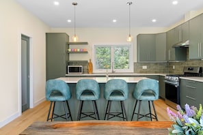 A modern kitchen with a central island, bar stools, and a window with a view of greenery.