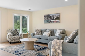 A living room with a sofa, armchairs, a coffee table, and a painting of a lake scene.