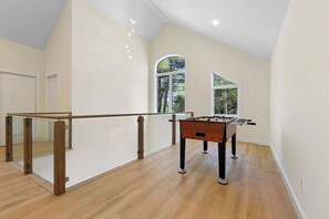 A spacious room with a wooden floor, a glass railing, and a foosball table.
