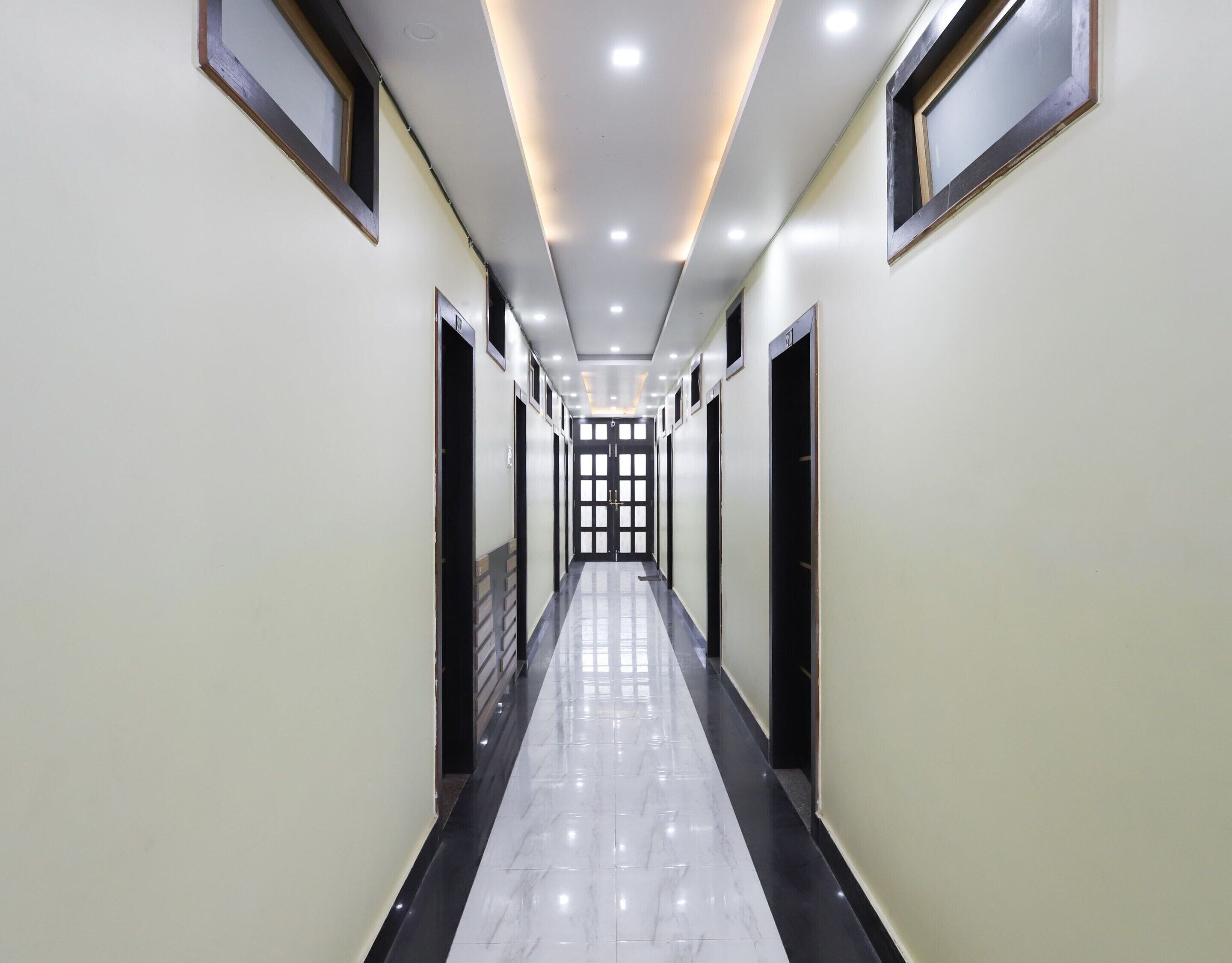 A long, narrow hallway with a shiny floor, doors on both sides, and a series of lights on the ceiling.