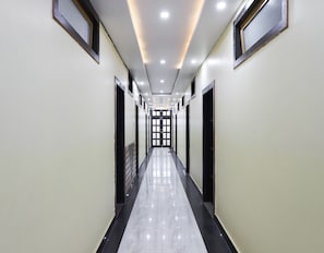 A long, narrow hallway with a shiny floor, doors on both sides, and a series of lights on the ceiling.