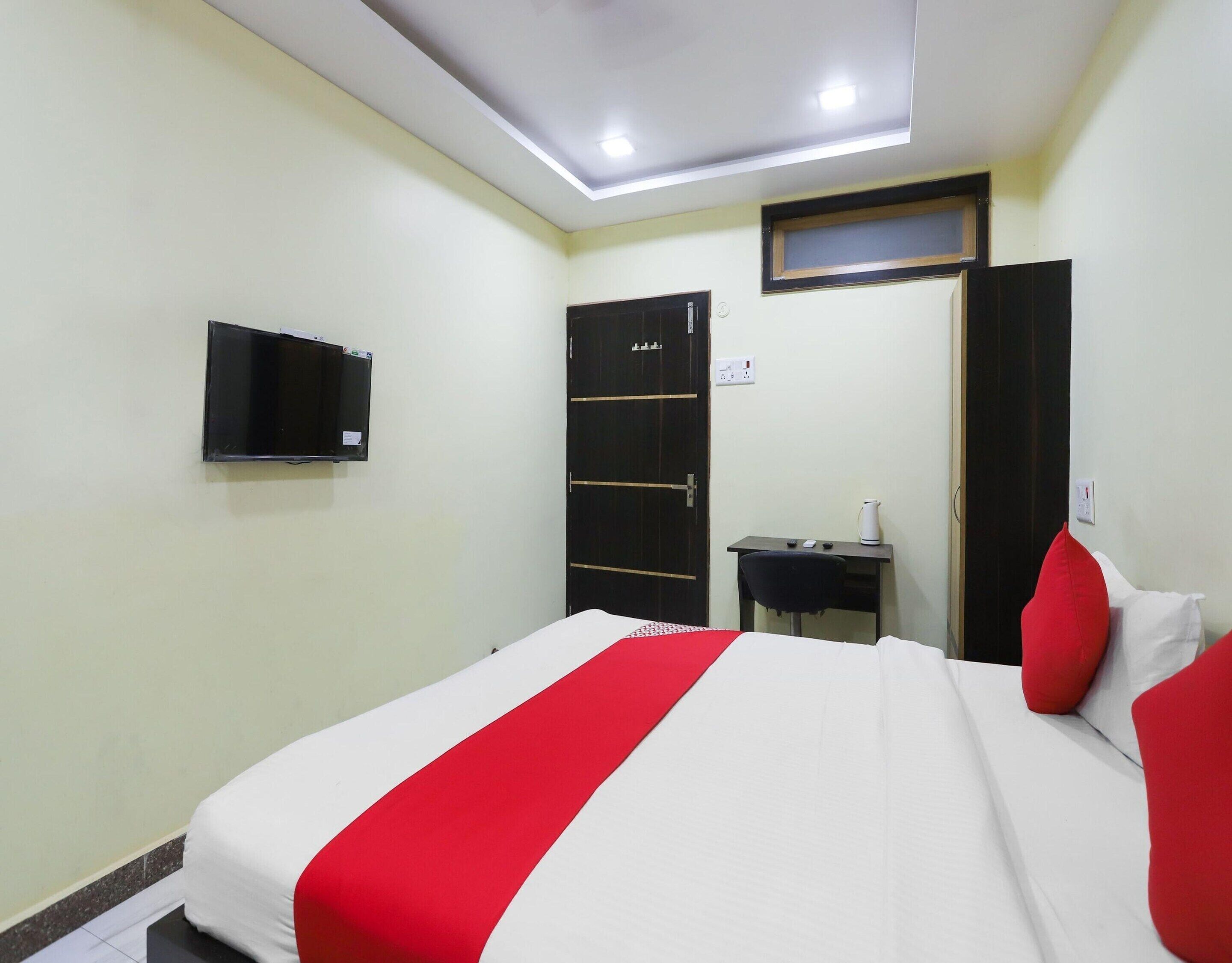 Quarto de hotel com cama, escrivaninha, televisão e guarda-roupa.