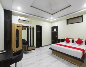 A hotel room with a bed, a desk, a chair, a wardrobe, and a mirror.
