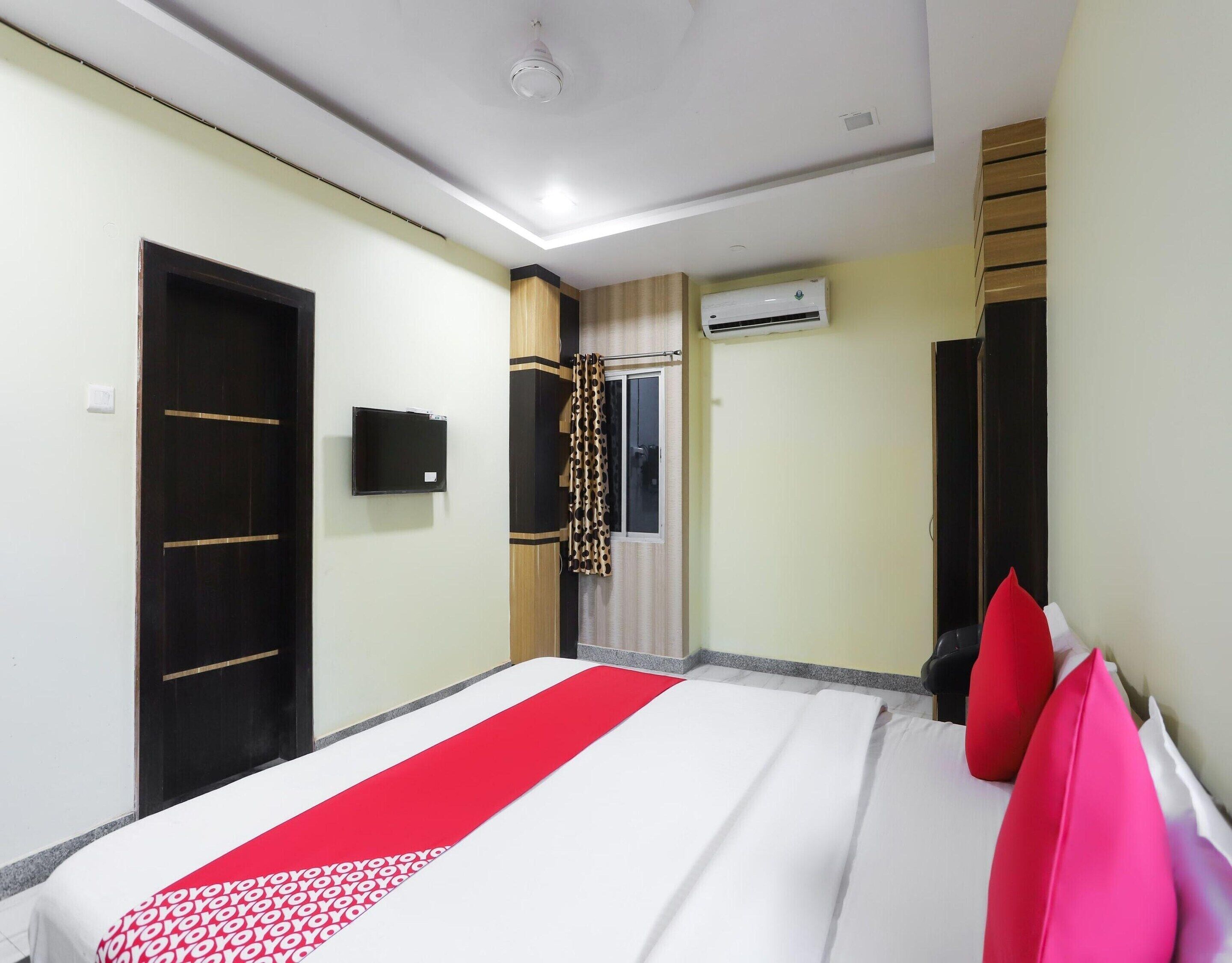 A hotel room with a bed, a wardrobe, a television, an air conditioning unit, and a window with curtains.