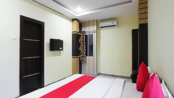 A hotel room with a bed, a wardrobe, a television, an air conditioning unit, and a window with curtains.