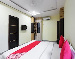 A hotel room with a bed, a wardrobe, a television, an air conditioning unit, and a window with curtains.