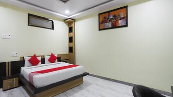 A hotel room with a bed, bedside tables, a chair, a painting on the wall, and a ceiling light.