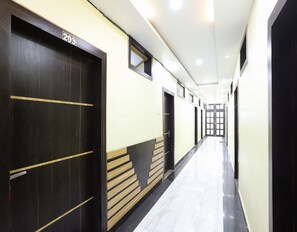 A hallway with doors marked with numbers, a tiled floor, and a light-colored wall. - Deluxe Akhand Param (Begusarai)