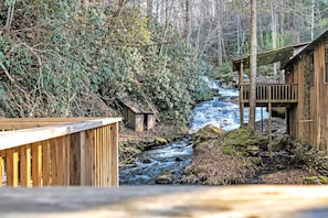 Una baita di legno con veranda in legno, circondata da una fitta foresta e un ruscello.