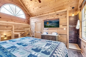 Une chambre dans une cabane en bois, avec un lit, un tableau, une fenêtre et une cheminée.