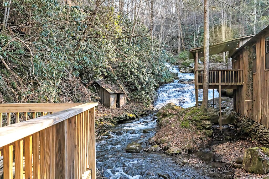 A wooden cabin with a wooden deck and a small waterfall in the background.