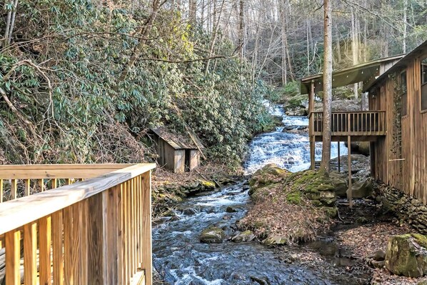 Une cabane en bois avec une terrasse en bois et une petite cascade en arrière-plan.