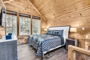 A wooden cabin bedroom with a bed, bedside tables, and a window.