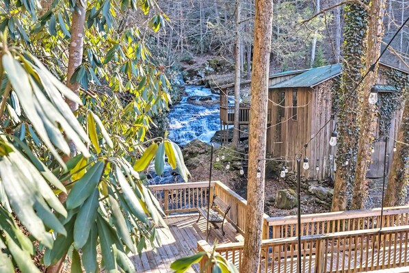 A wooden deck overlooking a stream with a wooden cabin and a bench.