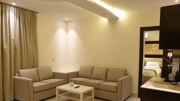 Una habitación de hotel moderna con un conjunto de sofá color beige, una mesa de centro blanca y un pequeño escritorio con lámpara.