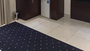 Habitación de hotel compacta con kitchenette, televisor de pantalla plana y alfombra oscura.