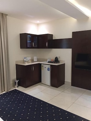 A compact hotel room with a kitchenette, a flat-screen TV, and a dark-colored rug. - Layali Lamar Hotel (Jeddah)