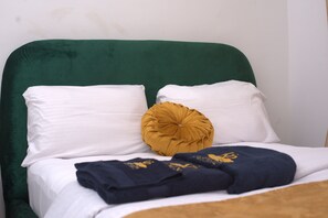 Un lit avec une literie blanche et une tête de lit recouverte d’un tissu vert.