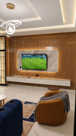 Un salon moderne avec un téléviseur à écran plat fixé à un mur en bois, un luminaire au plafond et un coin salon agrémenté d’un tapis à motifs.