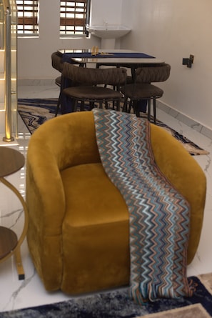 Une pièce avec un fauteuil jaune, une table à manger avec des chaises, un évier blanc et un tapis à motifs.