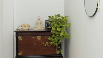 A corner room with a dark wooden dresser, a small Buddha statue, a vintage telephone, and a green plant.