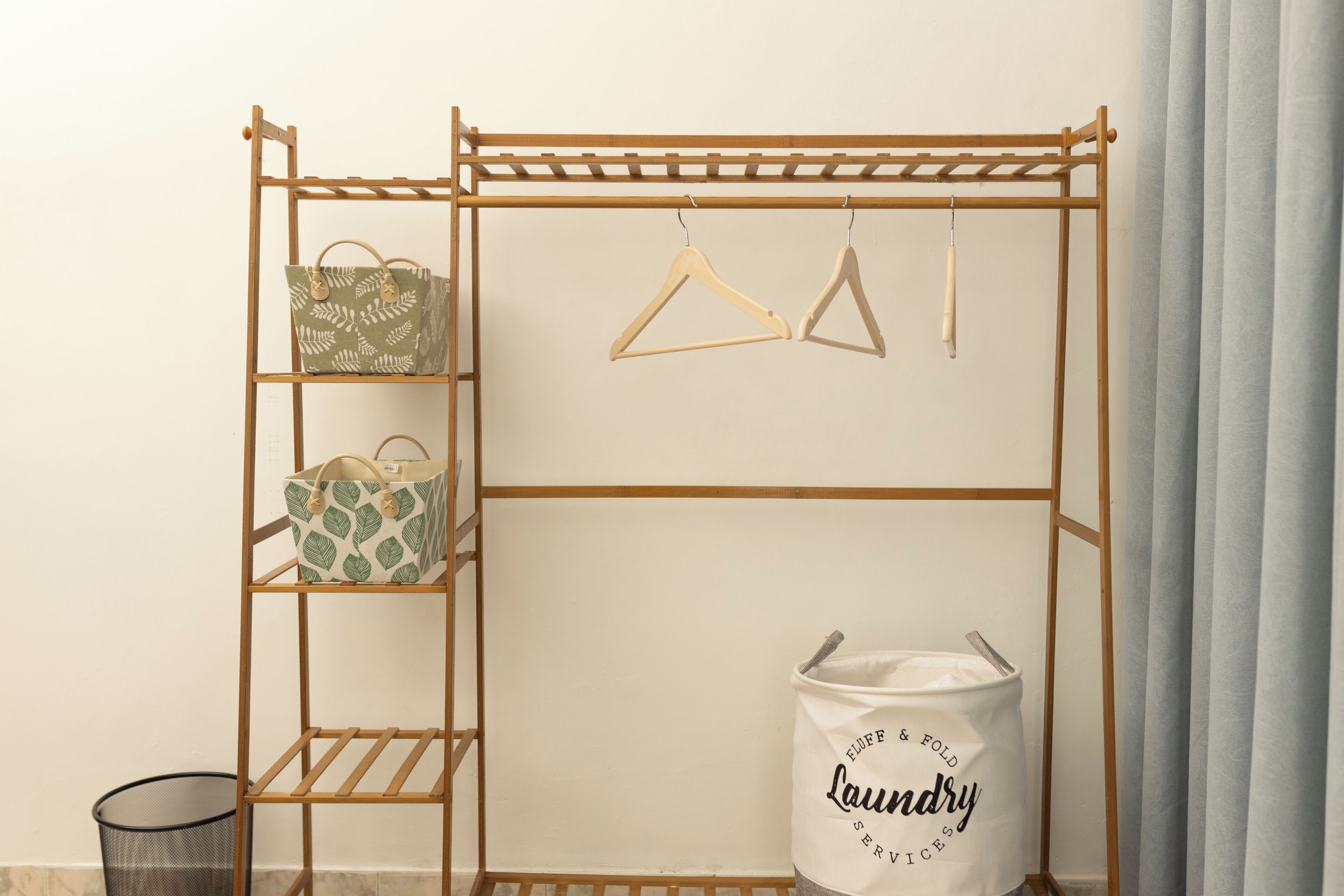 A wooden drying rack with hangers and bags, a trash bin, and a bag labeled 'Laundry Services'.