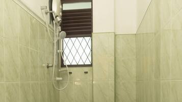 A bathroom with green tiles, a shower, a toilet, and a window with a metal grate.