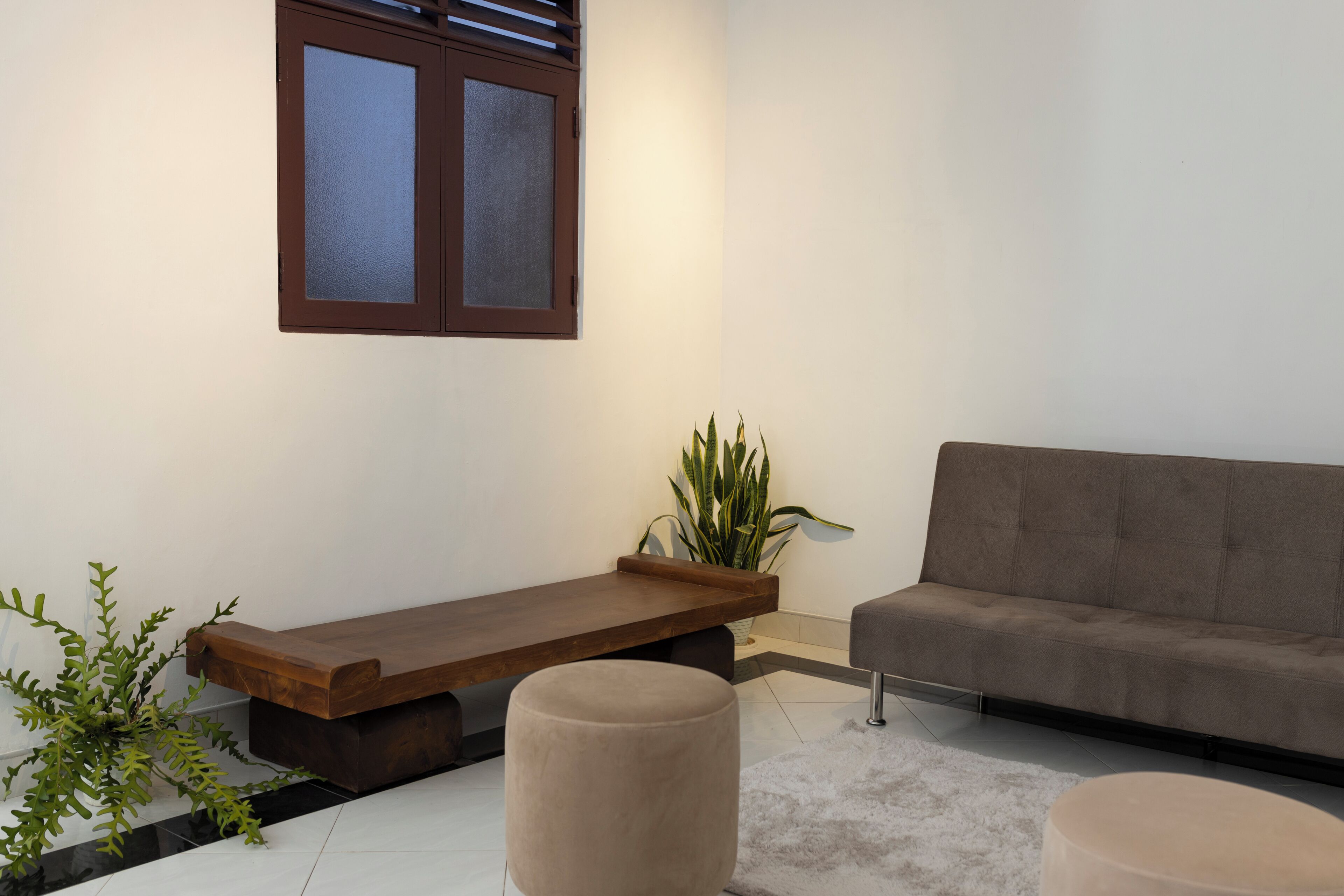 A modern living room with a wooden bench, a grey sofa, and a round ottoman.