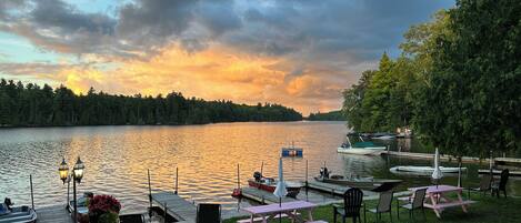 A lakeside view with docked boats, picnic tables, and chairs.