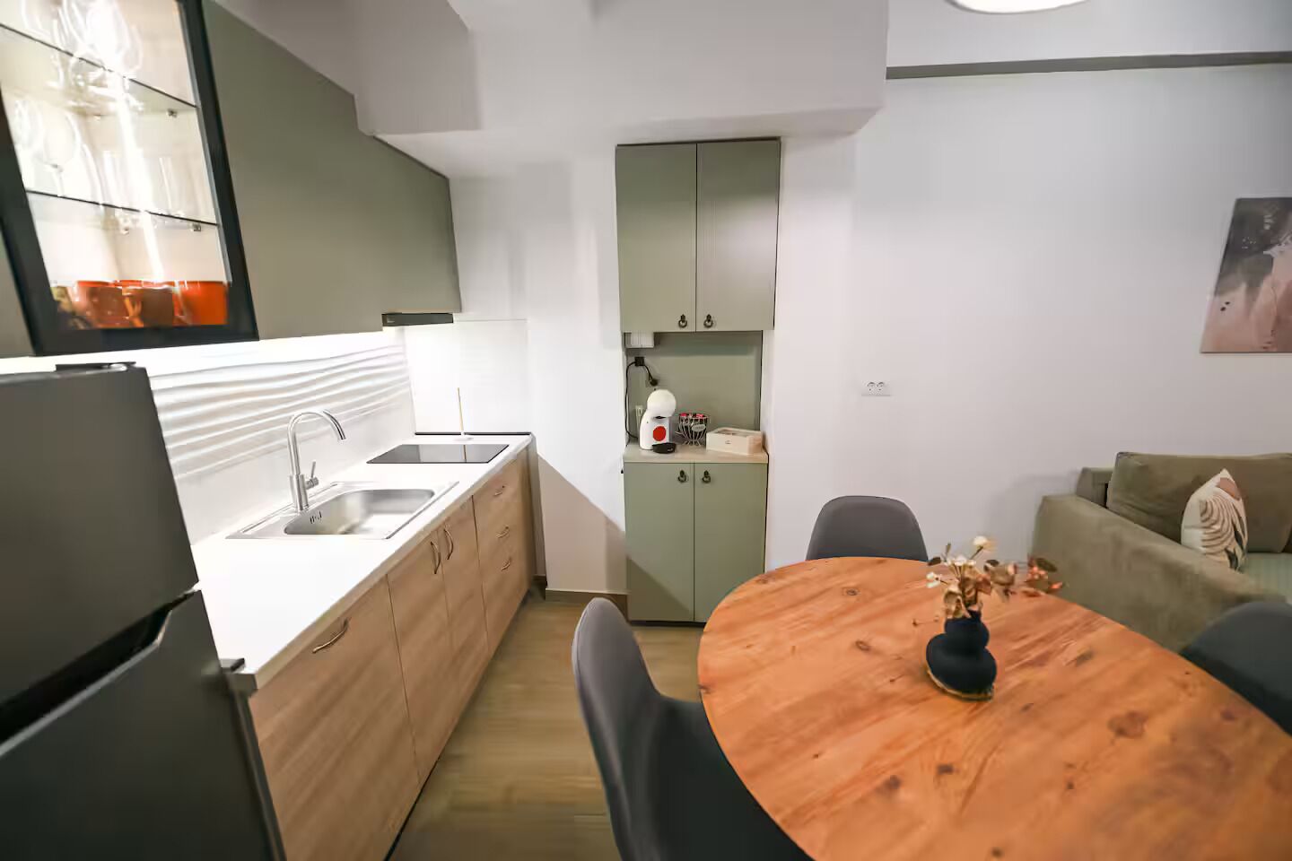 A modern kitchen with a wooden dining table, a refrigerator, and a sink.