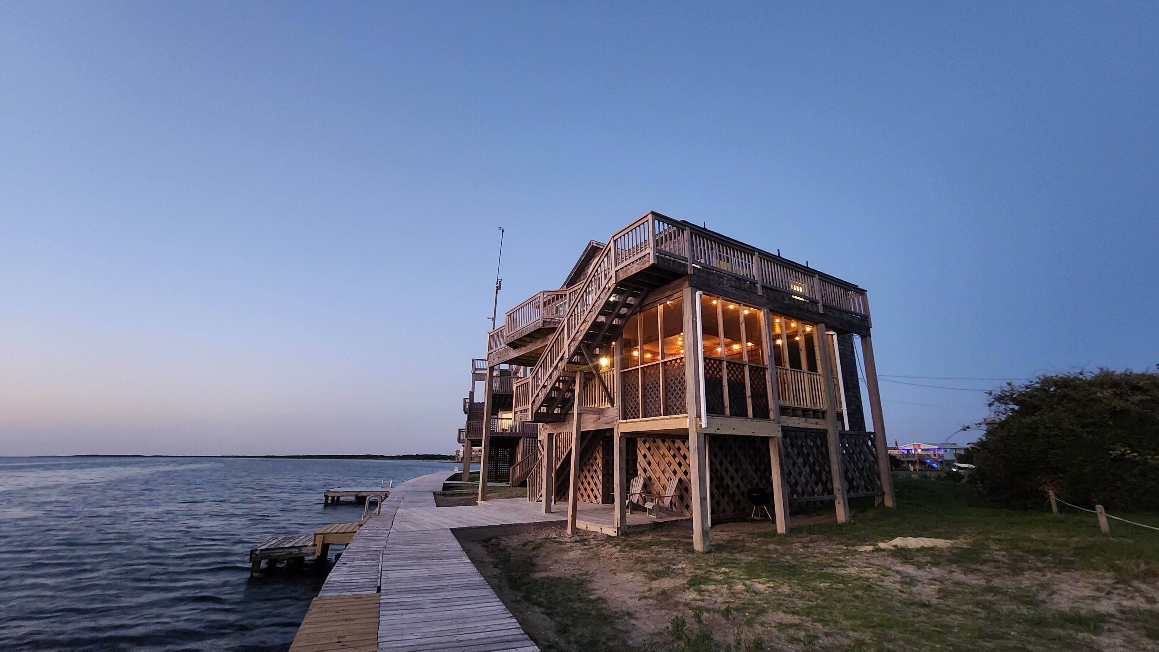A wooden structure with a deck extending over water, featuring a staircase and outdoor seating.