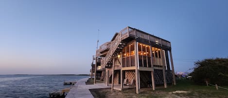 A wooden structure with a deck extending over water, featuring a staircase and outdoor seating.