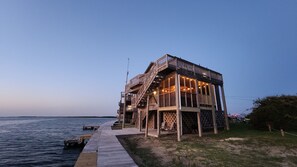 A wooden structure with a deck extending over water, featuring a staircase and outdoor seating. - Pet-Friendly Soundfront Retreat with Private Dock & Incredible Sunsets. (Avon)