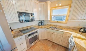 A compact kitchen with white cabinets, a built-in oven, a microwave, and a window providing natural light. - Pet-Friendly Soundfront Retreat with Private Dock & Incredible Sunsets. (Avon)