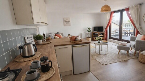 Eine moderne Küche mit einer Kaffeestation, einem kleinen Kühlschrank und einem Essbereich mit einer Couch und einem Fernseher.