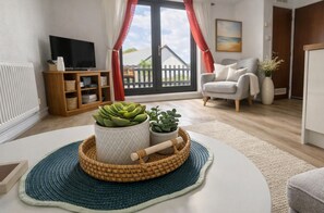 Uma sala de estar com um sofá branco, uma televisão, um armário de madeira e uma grande janela com cortinas.