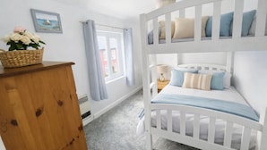Ein Etagenbett mit Kissen, eine Holzkommode, ein Blumenkorb, ein Fenster mit Vorhängen und ein Gemälde an der Wand.