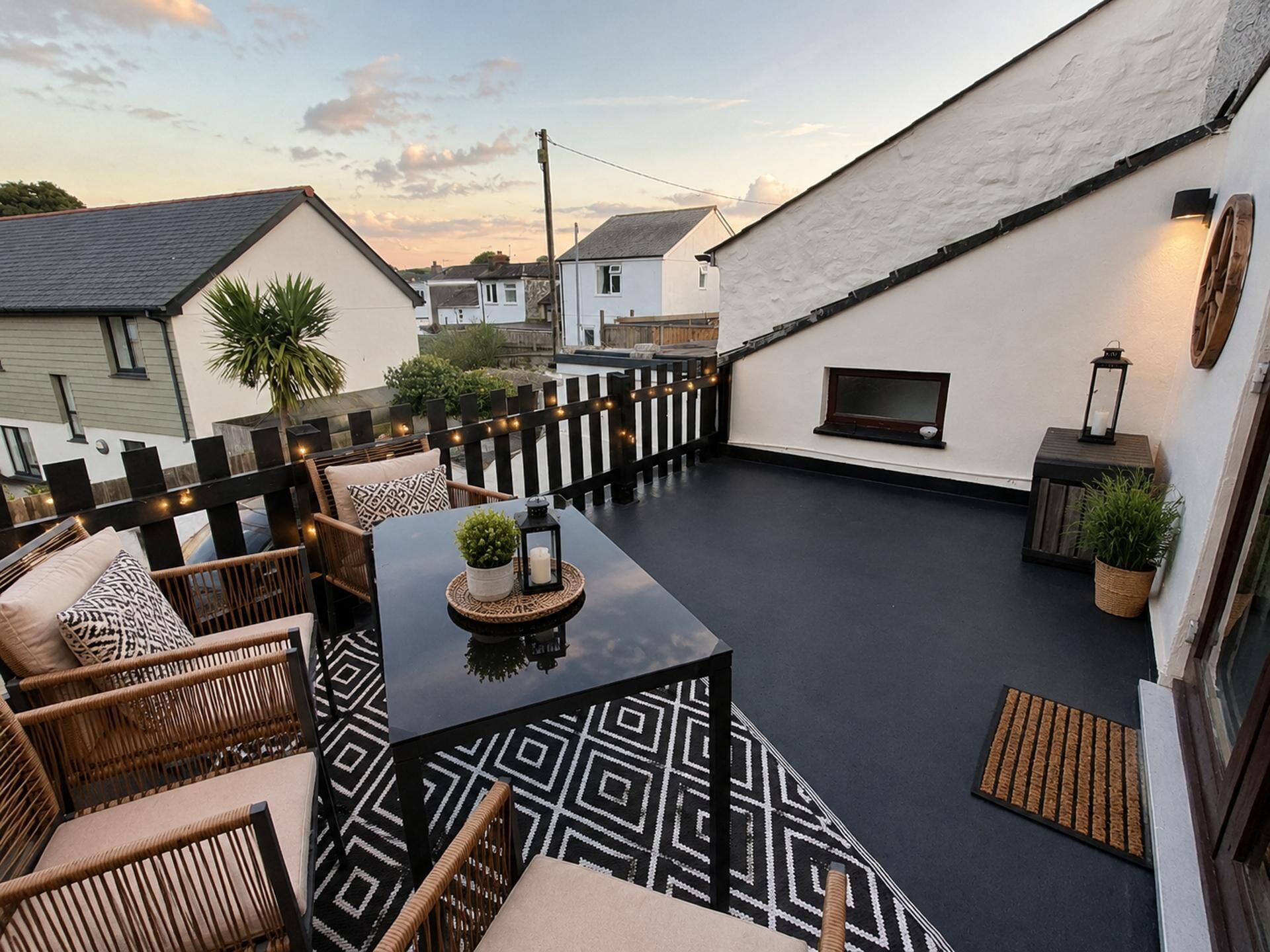 A rooftop patio with a black table, wicker chairs, and a TV screen.