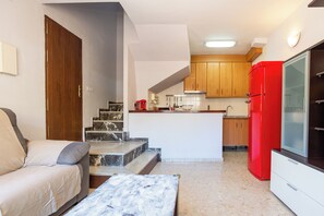Ein kompakter Wohnbereich mit Sofa, Couchtisch, Küchenzeile mit Holzschränken und einem roten Kühlschrank, sowie einer Treppe zu einer oberen Ebene.