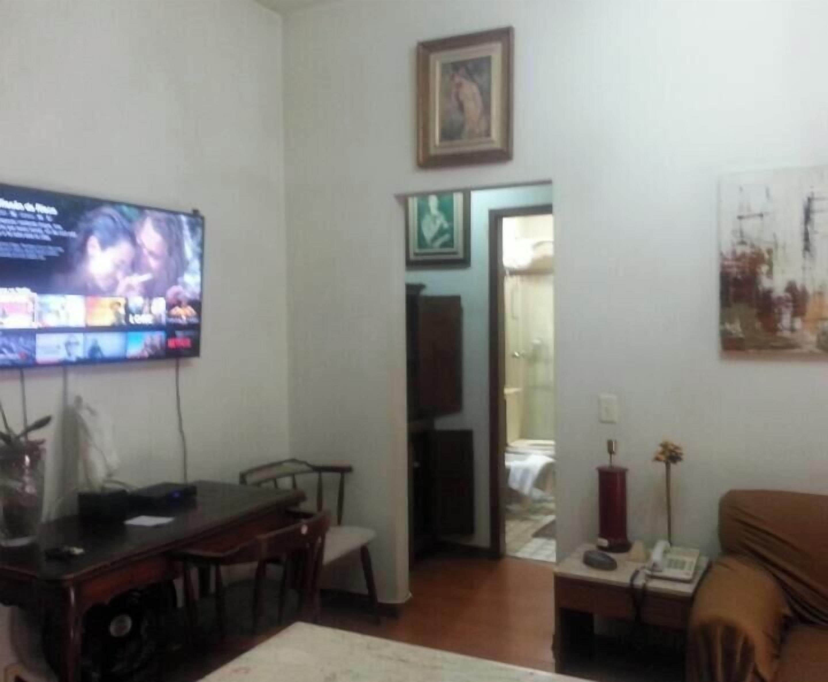 A living room with a television, a dining table, chairs, a sofa, and artwork on the walls.