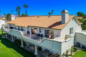 A two-story house with a covered patio, a chimney, and a view of palm trees. - Wilson's Desert Oasis - Beautiful 3-bdrm condo in Palm Desert with AC, amenities (Palm Desert)