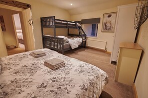 Une chambre avec un lit superposé, un lit simple avec une literie à motifs floraux, un radiateur et une porte donnant sur une autre pièce.
