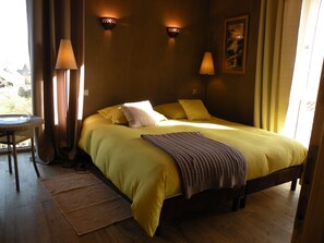 Una stanza con un letto, due lampade a parete, un tavolino con una sedia e una finestra con tende.
