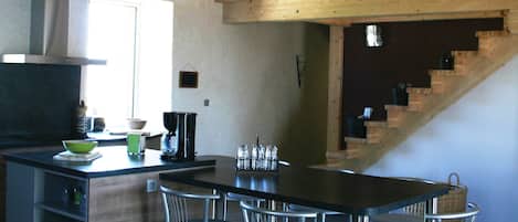 A modern kitchen with a large island, stainless steel chairs, and hanging pendant lights.