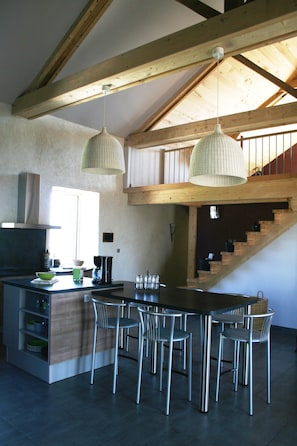 A modern kitchen with a large island, stainless steel chairs, and hanging pendant lights.