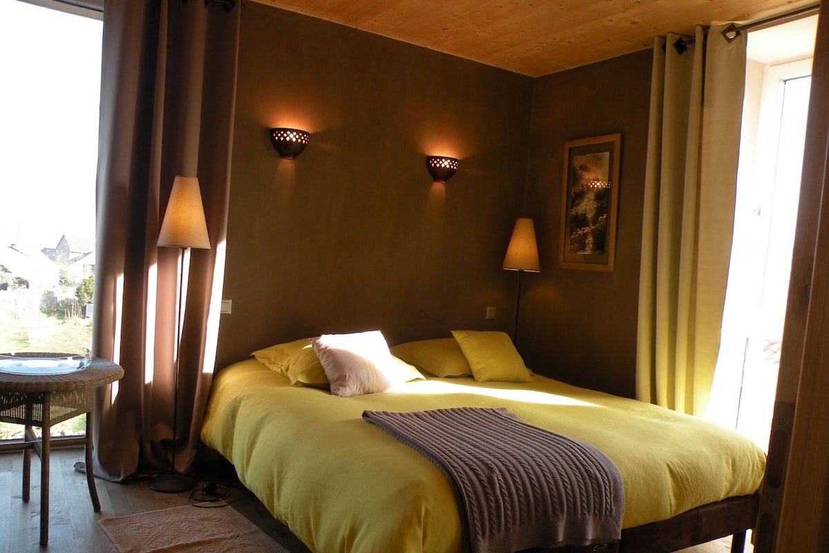A bedroom with a bed, two wall-mounted lamps, a window with curtains, and a small table with a chair.