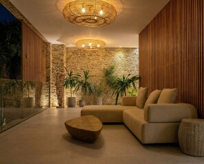 A modern living room with a stone wall, a large sofa, a coffee table, and a hanging light fixture. - Villa OASIS - Jeri (Jijoca de Jericoacoara)