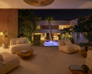 A modern lounge area with a pool, comfortable seating, and a view of a multi-level building at night. - Villa OASIS - Jeri (Jijoca de Jericoacoara)