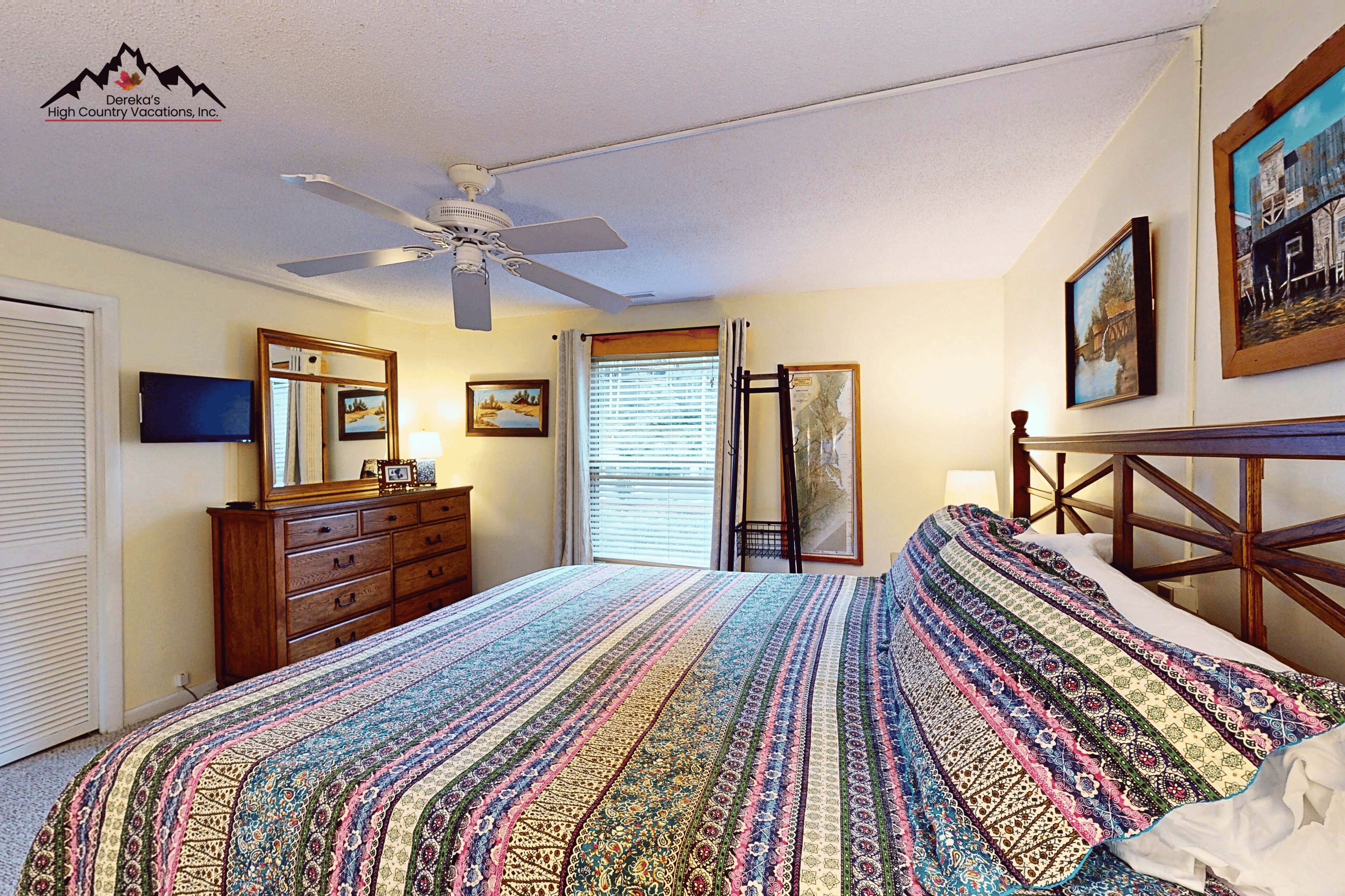 A bedroom with a bed, dresser, ceiling fan, and a painting on the wall.